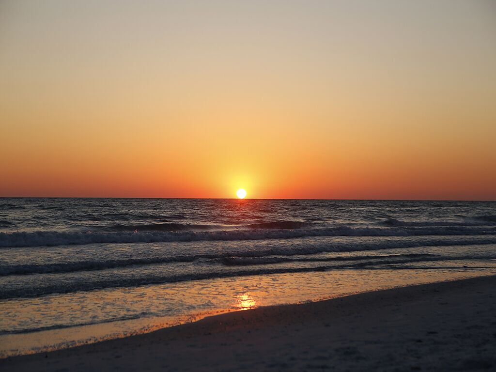 A sunset over the ocean with waves on a beach.