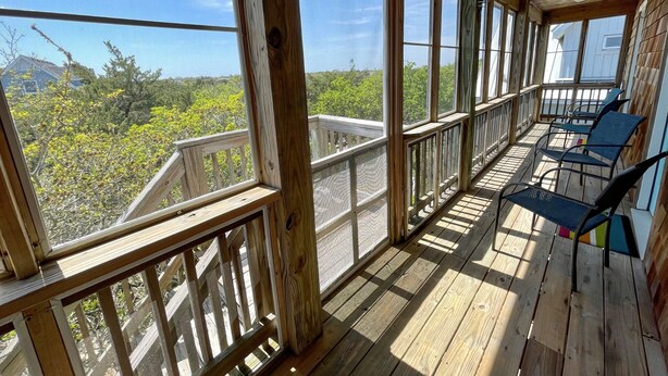 Een houten terras met een balustrade, grote ramen en buitenmeubels.