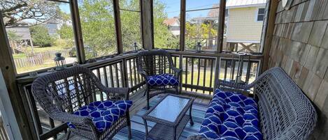 A covered porch with wicker furniture and a striped rug.