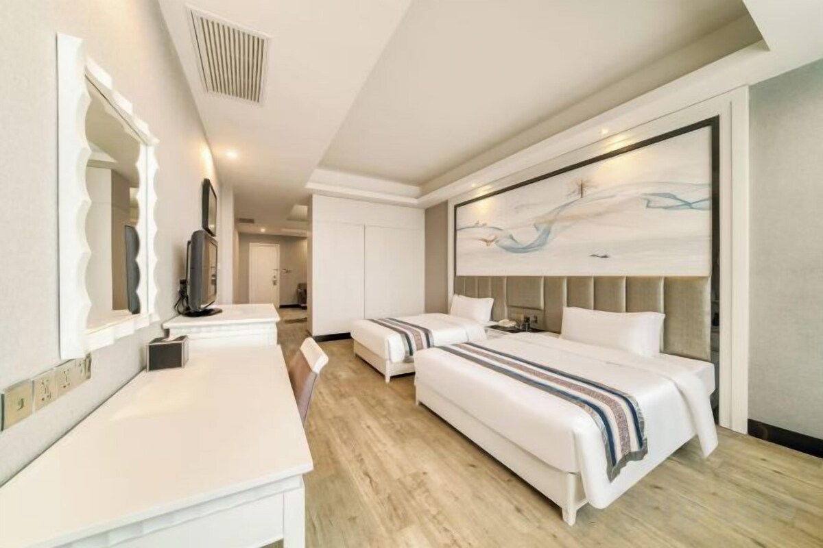A modern hotel room with a large bed, a separate seating area, and a large artwork on the wall.