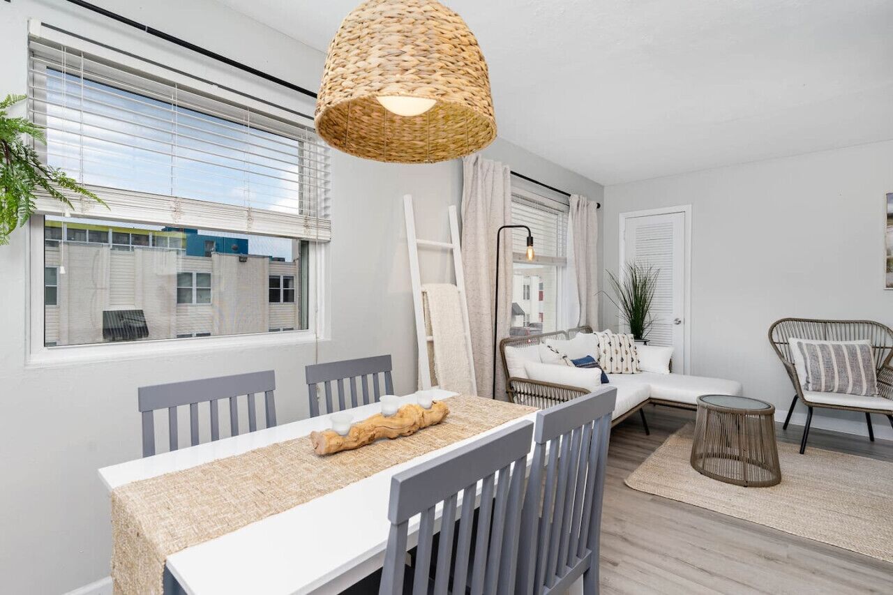 A modern living room with a dining area, featuring a large window, a woven light fixture, a sofa, and a chair.