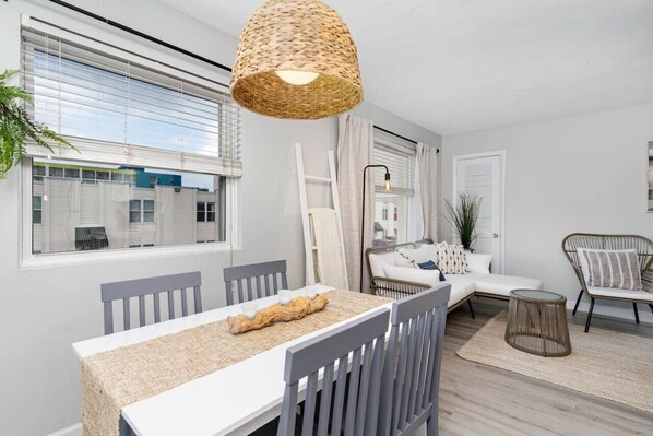 A modern living room with a dining area, featuring a large window, a woven light fixture, a sofa, and a chair.