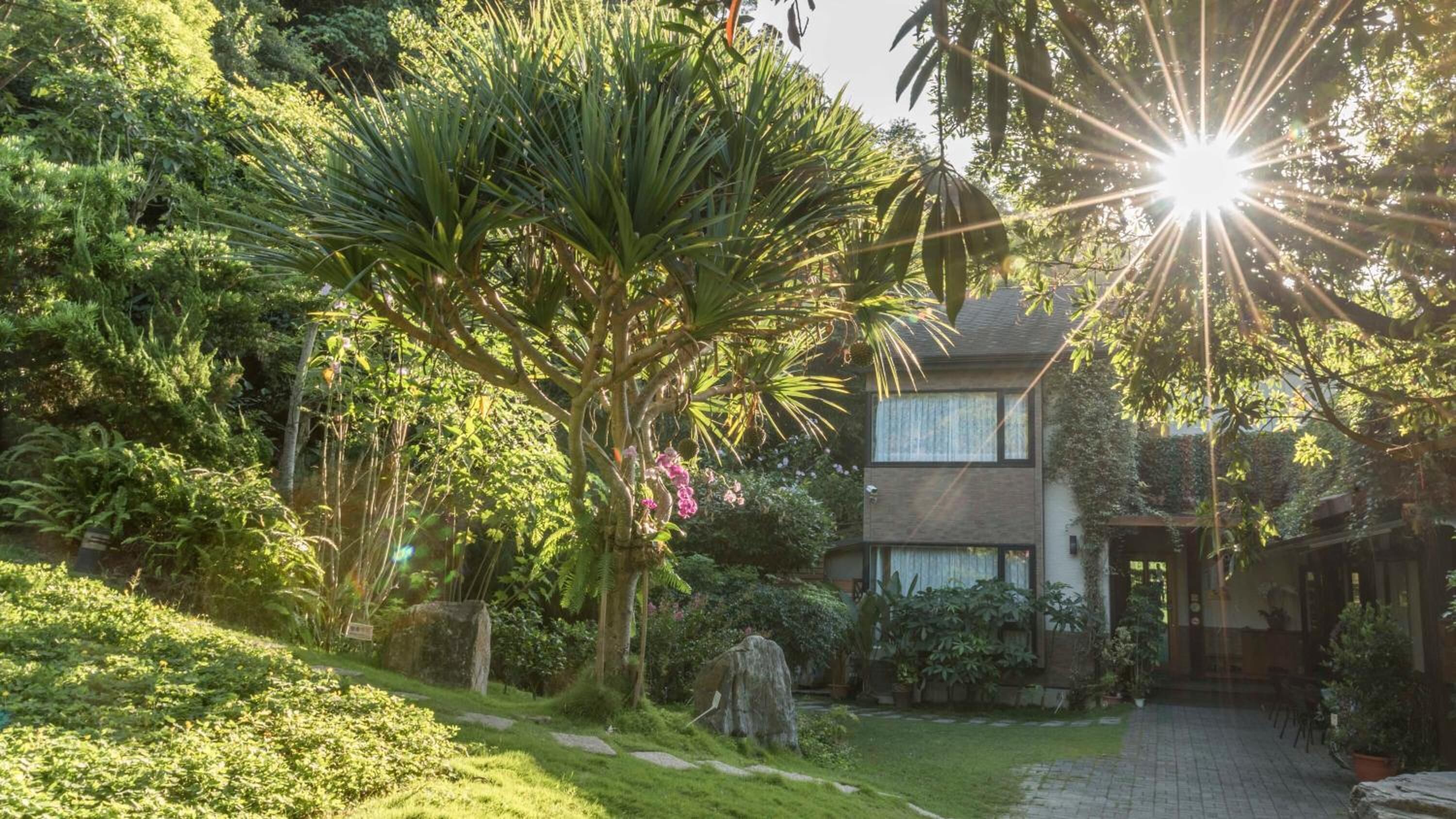 A two-story house with a garden, a pathway, and a stone wall.