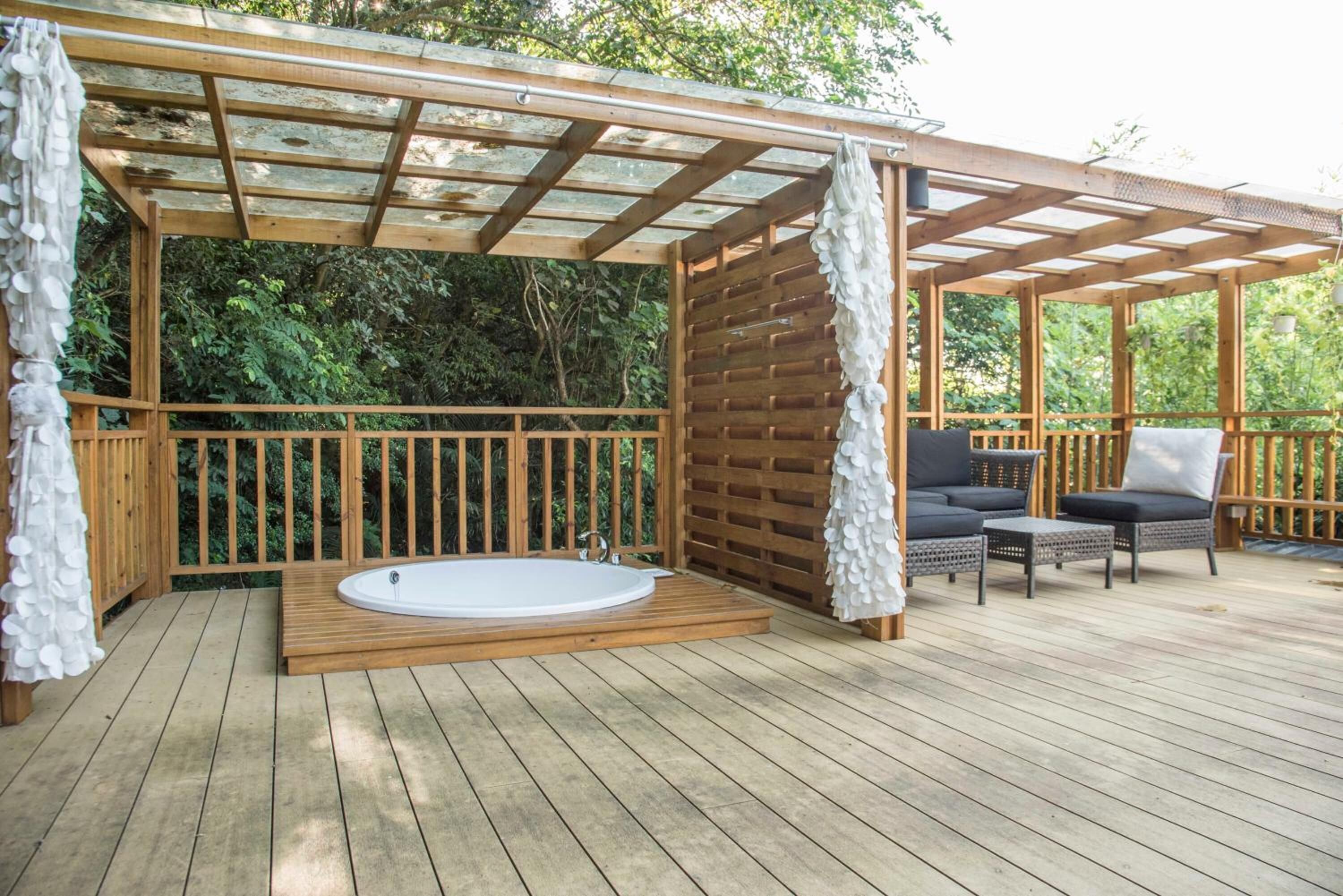 A wooden deck with a hot tub, outdoor seating, and a pergola.