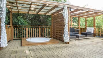 A wooden deck with a hot tub, outdoor seating, and a pergola.
