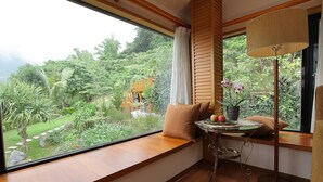 A room with a large window offering a view of a lush garden and a wooden staircase. - Crossing The Rainbow Bridge B&B (Xiulin)