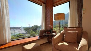 A room with a large window offering a view of a bridge and greenery, a sofa, a small table with a lamp, and a decorative plant. - Crossing The Rainbow Bridge B&B (Xiulin)
