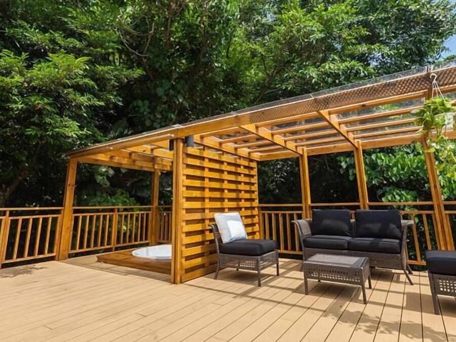 A wooden deck with a pergola, two black wicker sofas, and a small table.