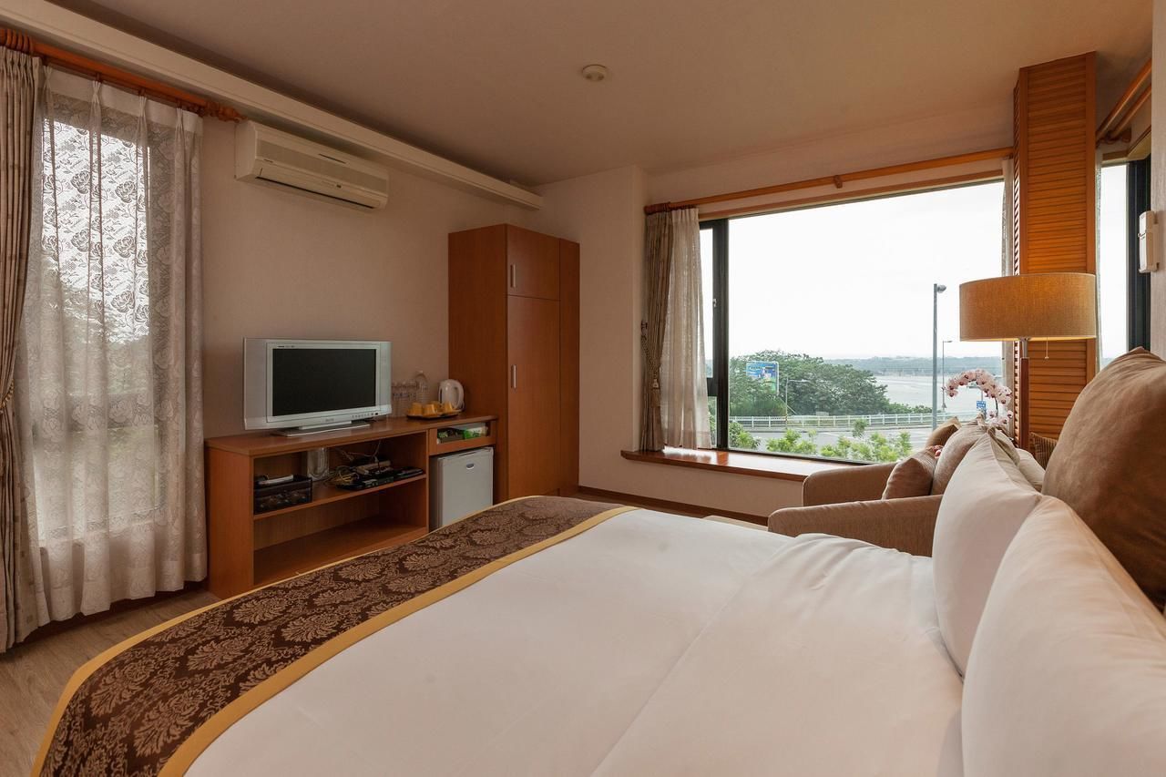 Quarto de hotel com cama, televisão, escrivaninha e janela com vista.