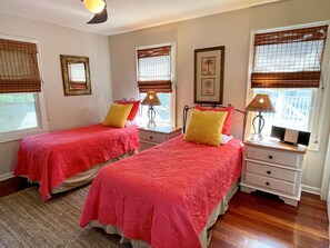 A bedroom with two beds, each with a red bedspread and a yellow pillow. There are bedside tables with lamps and a framed picture on the wall. - Redbeard's Claim: Professionally decorated, perfect relaxing island home. (Ocracoke)