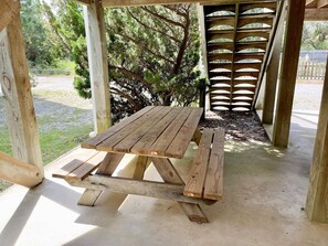 A wooden picnic table under a wooden pergola with a lattice backrest, set on a concrete patio with a grassy area and trees in the background. - Redbeard's Claim: Professionally decorated, perfect relaxing island home. (Ocracoke)