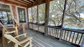 Une véranda en bois offre une vue sur un lac et des arbres. On y trouve des chaises et une table en bois.