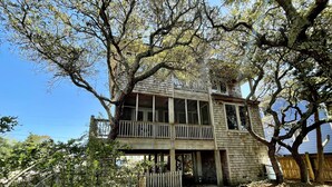 Une maison en bois à deux étages, dotée d’un balcon et entourée d’arbres et d’une clôture en bois.