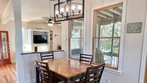 Un coin repas avec une table et des chaises en bois, un ventilateur de plafond et une grande fenêtre donnant sur l’extérieur.