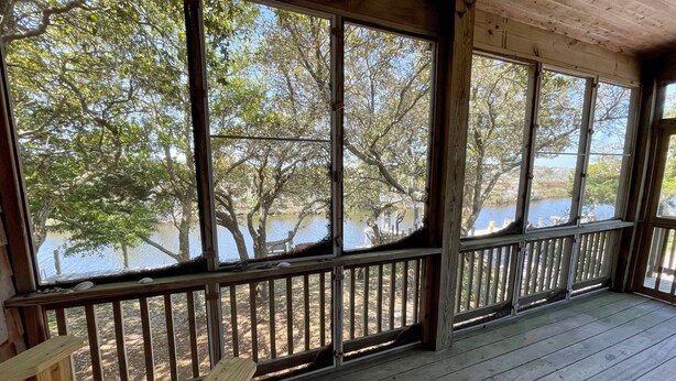 Une terrasse en bois avec une rambarde donnant sur une étendue d’eau et des arbres.