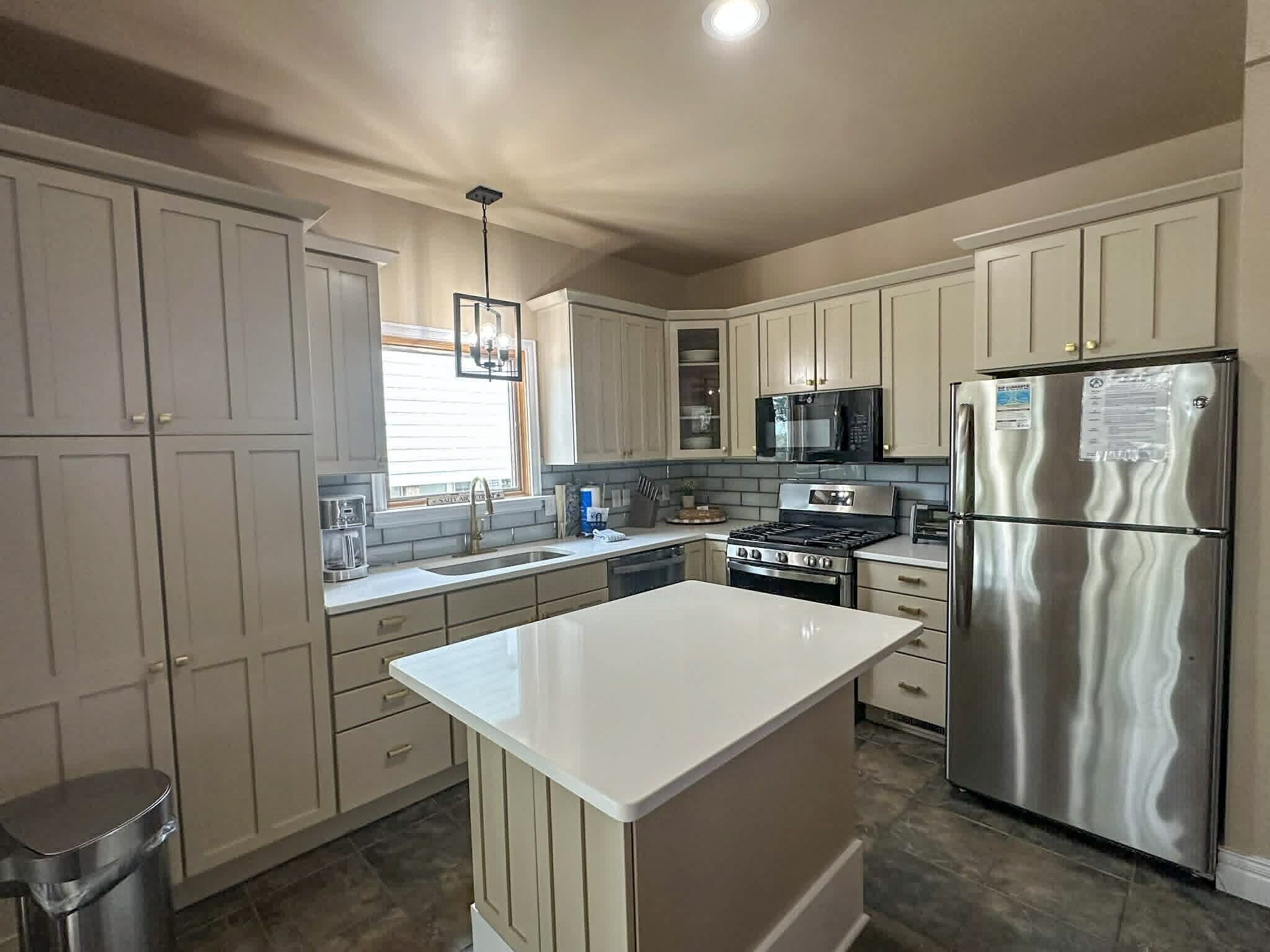 A kitchen with white cabinets, stainless steel appliances, a central island, and a window with blinds.