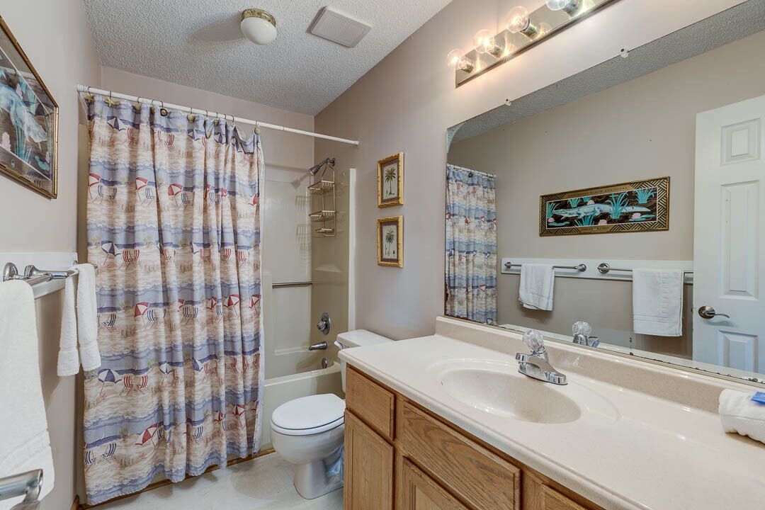 Een badkamer met een bad, toilet en wastafel. Handdoeken hangen aan de muur en er is een douchegordijn met een nautisch thema.