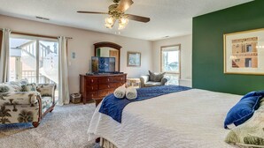 A bedroom with a large bed, a ceiling fan, a dresser, a chair, and a view of the outside.