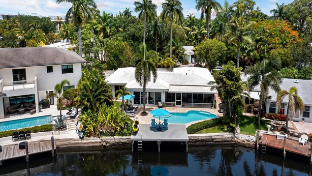 A residential area with a swimming pool, a dock, and a house surrounded by palm trees.