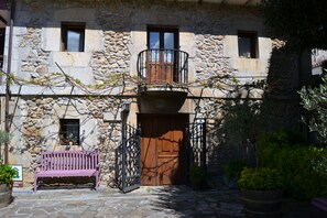 A stone building with a wooden door, a balcony, and a bench. - Posada Soano (Arnuero)