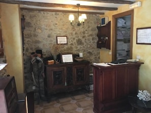 A rustic room with stone walls, a wooden reception desk, and a chandelier. - Posada Soano (Arnuero)