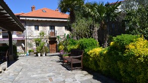 A stone pathway leading to a stone building with a red-tiled roof, surrounded by lush greenery and a bench. - Posada Soano (Arnuero)