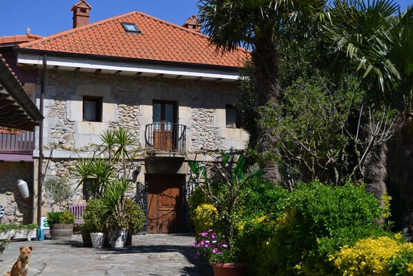 A stone building with a red-tiled roof, a wooden door, and a balcony with a metal railing. - Posada Soano (Arnuero)