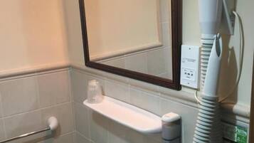 Une salle de bain avec un lavabo blanc, un miroir, un porte-serviettes, un sèche-cheveux et une petite étagère sur laquelle se trouvent un verre et un récipient.