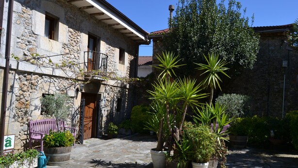 A stone building with a balcony, potted plants, and a stone-paved courtyard. - Posada Soano (Arnuero)