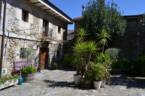 A stone building with a balcony, potted plants, and a stone-paved courtyard. - Posada Soano (Arnuero)
