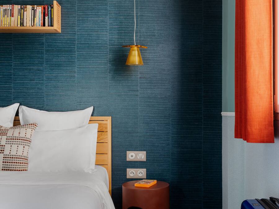 Una habitación de hotel moderna con una cama de madera, una estantería, un taburete redondo peculiar y una maleta.