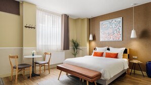 Een moderne hotelkamer met een groot bed, een bankje, twee stoelen, een kleine tafel en een plant in pot.