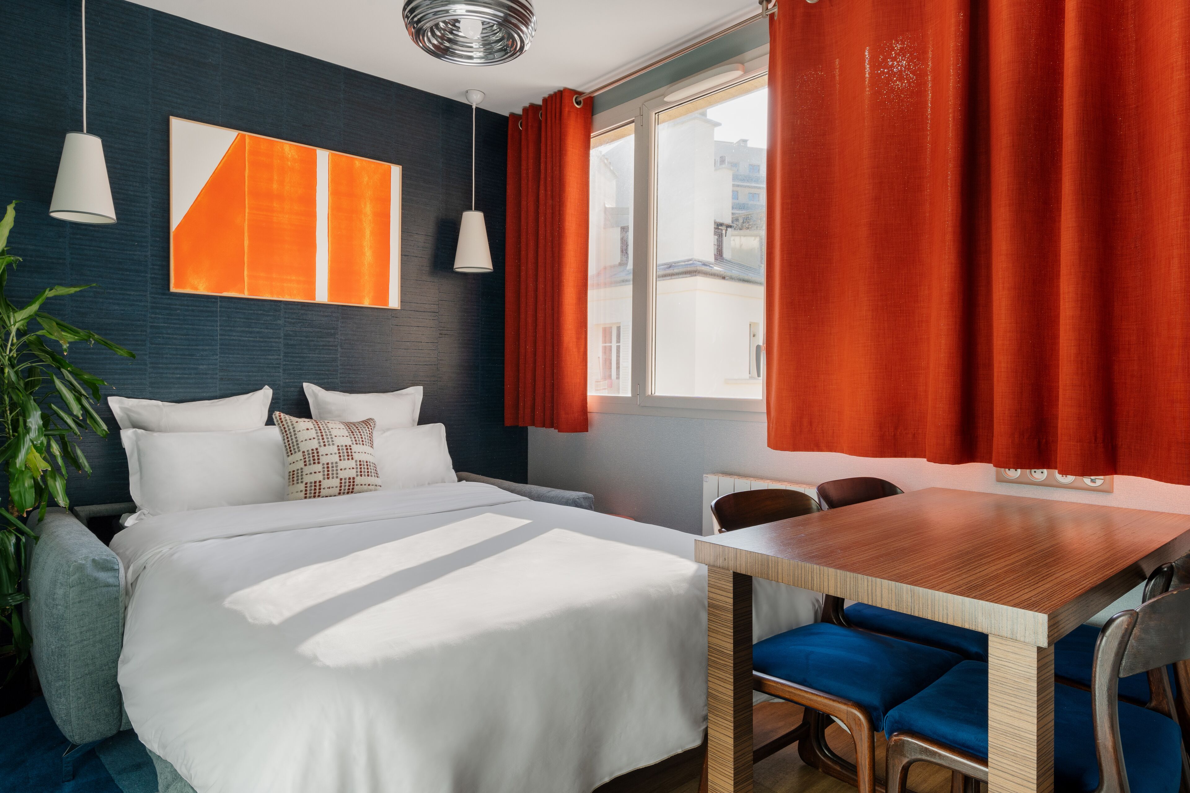 Ein modernes Hotelzimmer mit einem großen Bett, einem Holztisch und Blick auf die Stadt durch ein großes Fenster.