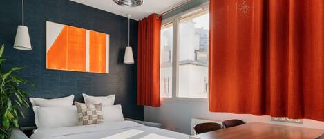 Ein modernes Hotelzimmer mit einem großen Bett, einem Holztisch und Blick auf die Stadt durch ein großes Fenster.