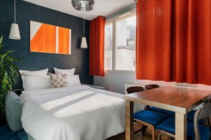Et moderne hotelværelse med en stor seng, et træbord og udsigt over byen gennem et stort vindue.