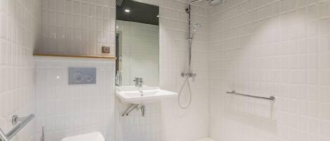 A modern bathroom with white tiled walls, a toilet, a sink, and a shower.