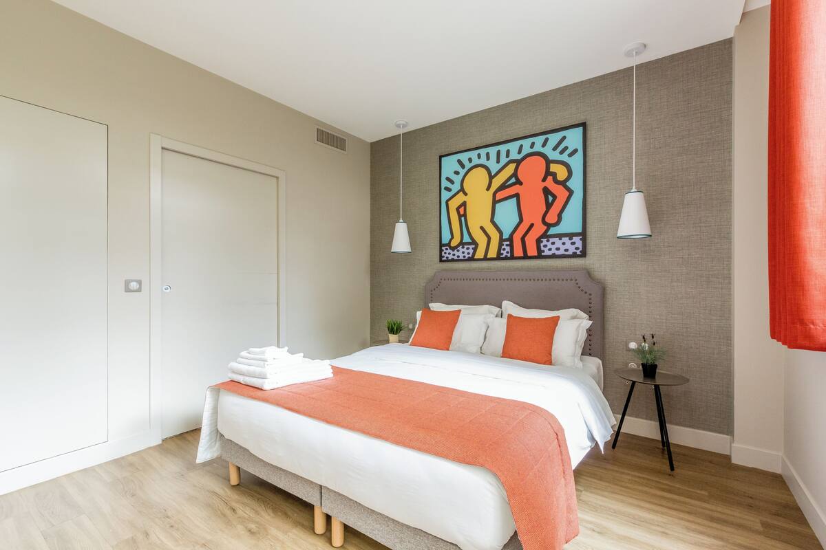 Un dormitorio moderno con una cama, una mesita de noche, una obra de arte en la pared y una cortina roja.