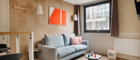 A modern living room with a grey sofa, a coffee table, and a dining area with a table and chairs.