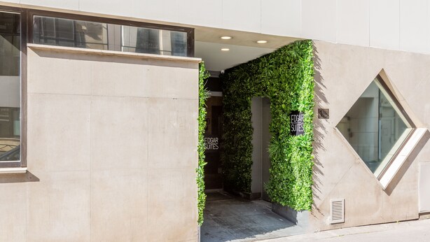 Een hotelentree met een modern ontwerp, met een betonnen gevel, een glazen deur en een verticale groene geveltuin.