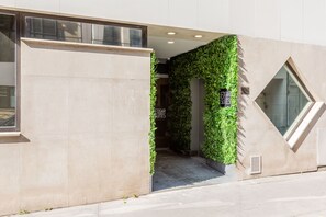 Entrada de hotel com design moderno, incluindo fachada de concreto, porta de vidro e jardim vertical verde.