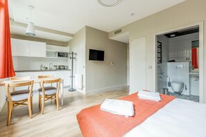 Et moderne hotelværelse med seng, et skrivebord med stole, et tekøkken og et badeværelse, der kan ses igennem en åben dør.