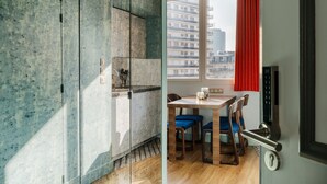 Een moderne keuken met een ingebouwde kookplaat, een eethoek met een houten tafel en blauwe stoelen, en uitzicht op een stadsbeeld door een raam met rode gordijnen.