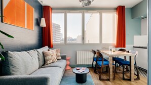 Een moderne woonkamer met een grijze bank, een ronde salontafel en een eethoek met een houten tafel en blauwe stoelen.