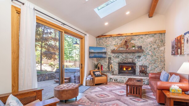 A spacious living room with a stone fireplace, a leather sofa, a wooden coffee table, and a large window overlooking a deck. - Large fenced yard with Hot Tub, Serene and quiet. (Carnelian Bay)