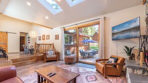 A spacious living area with a wooden coffee table, leather sofa, and a large sliding glass door leading to an outdoor patio. - Large fenced yard with Hot Tub, Serene and quiet. (Carnelian Bay)