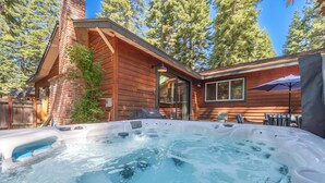 A hot tub with a wooden deck and a brick chimney, surrounded by trees and a clear sky. - Large fenced yard with Hot Tub, Serene and quiet. (Carnelian Bay)