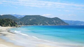 A beach with clear turquoise waters, sandy shore, and green hills in the background. - Pension A Million Roses (Shimoda)