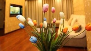 A room with a floral arrangement on a table, a sofa, and a television on the wall. - Yinhuang Holiday Hotel (Chengdu)