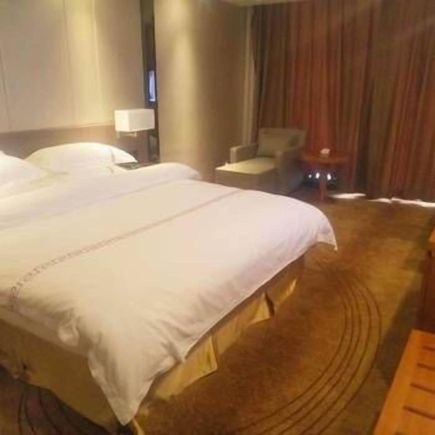 A hotel room with a large bed, a chair, a nightstand, and a lamp.