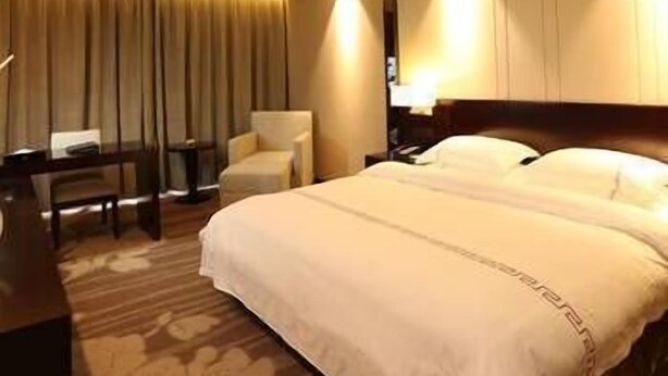 A hotel room with a large bed, a desk, a chair, and a lamp. - Yinhuang Holiday Hotel (Chengdu)
